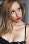 Retrato de modelo rubia con labios rojos y lencería negra, sobre fondo claro.