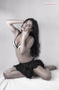 Modelo femenina sentada sobre fondo gris, en una pose íntima y serena.