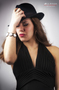 Modelo femenina con sombrero negro y ropa oscura, posando en estudio.