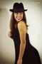 Modelo femenina con sombrero negro y vestido oscuro, posando de perfil.
