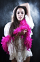 Modelo femenina con boa rosa, sentada sobre fondo claro en una imagen de moda.