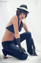 Modelo femenina con sombrero negro, sentada en cuclillas sobre fondo claro.