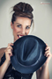 Modelo femenina sujetando un sombrero azul, con mirada directa.