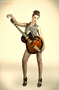 Modelo femenina con guitarra, posando de pie sobre fondo claro.