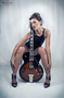 Modelo femenina sentada con instrumento musical sobre fondo claro.