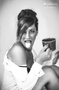 Retrato en blanco y negro de modelo femenina sonriendo con una cámara en la mano.