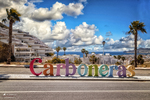 Cartel de Carboneras junto al paseo marítimo, con palmeras, cielo azul y ambiente costero de Almería.