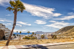 Paseo costero de Carboneras con palmera, carretera, mar azul y montañas al fondo.