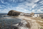 Vista de la costa de Carboneras con playa, formaciones rocosas, edificios blancos y cielo nublado.