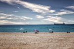 Playa de Carboneras con bañistas, mar azul y velero navegando en el horizonte mediterráneo.