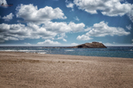 Vista de la playa de Carboneras con isla al fondo, cielo de grandes nubes y mar Mediterráneo.