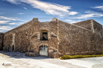 Edificio antiguo de piedra en Carboneras, con entrada oscura, cielo azul y paisaje urbano mediterráneo.
