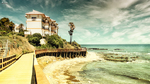 Camino junto a la costa de Mijas con pasarela elevada, playa rocosa y vivienda blanca frente al Mediterráneo.