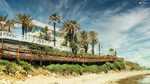 Jardines, palmeras y paseo junto al Sendero Litoral de Mijas, con playa y cielo azul en la Costa del Sol.