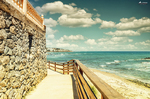 Paseo junto a muro de piedra en el Sendero Litoral de Mijas, con playa, mar azul y luz mediterránea.