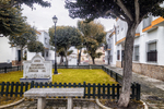 Pequeño jardín urbano en Rota, Cádiz, con bancos, árboles y casas blancas alrededor.