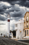 Faro o chimenea histórica en una calle de Rota, con edificios blancos y cielo dramático.