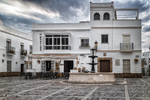 Edificio blanco en una plaza de Rota, con ventanas, bancos y arquitectura urbana gaditana.