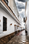 Calle estrecha de Rota con fachadas blancas, zócalo de piedra y suelo mojado.