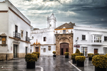 Iglesia blanca de Rota en una plaza, con maceteros, farolas y cielo nublado.