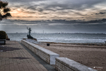 Paseo marítimo de Rota al atardecer, con mar Atlántico, playa y bancos frente al horizonte.
