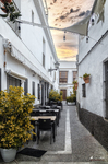 Rincón tranquilo de Rota con calle estrecha, bancos, macetas y paredes blancas.