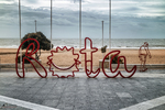 Cartel de Rota junto a la playa, con mar Atlántico al fondo y cielo nublado.