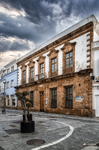 Edificio histórico de ladrillo en una calle de Rota, con farola y cielo nublado.