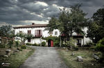 Casa rural blanca entre jardines en el norte de España, con camino de entrada, vegetación y cielo nublado.