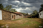 Edificio de piedra en un entorno rural del norte de España, con pradera y nubes de tormenta.