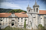 Iglesia o monasterio con torres de piedra en el norte de España, rodeado de paisaje verde.