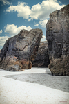Grandes paredes de roca en la Playa de las Catedrales, con arena blanca y cielo azul entre los acantilados.