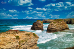 Rocas monumentales de la Playa de las Catedrales rodeadas por el oleaje, con cielo azul y nubes blancas.