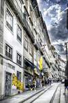 Calle del centro de Oporto con edificios altos, comercios y banderas en fachadas históricas.