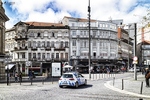 Plaza urbana de Oporto con edificios históricos, tráfico y cielo nublado sobre la ciudad.