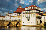 Edificio blanco junto al río Támega en Chaves, con puente, arquitectura histórica y nubes de tormenta.