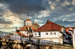 Vista de Chaves junto al río Támega, con edificios históricos, puente y cielo dramático al atardecer.
