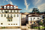 Edificio blanco con tejado rojo junto al río Támega en Chaves, Portugal, bajo cielo azul.