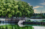 Orilla ajardinada del río Támega en Chaves, con árboles reflejados en el agua.