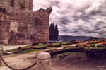 Restos históricos de piedra en Chaves, con sendero, jardines y nubes sobre el casco antiguo.