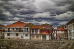 Edificios residenciales de Chaves bajo un cielo tormentoso, con tejados rojos y fachadas claras.