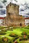 Torre medieval en los jardines de Chaves, Portugal, rodeada de césped y flores.