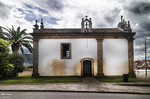 Capilla blanca en Chaves, Portugal, con espadaña, puerta verde y cielo nublado.