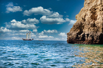 Vista de la costa de Lagos desde el mar con rocas, cuevas y cielo despejado.