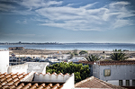 Vista elevada de Lagos con tejados blancos, puerto y horizonte marítimo al fondo.