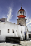 Faro blanco y rojo de Lagos, Portugal, con cielo azul y nubes verticales.