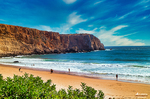 Playa del Algarve rodeada de acantilados rojizos y vegetación bajo un cielo azul intenso.