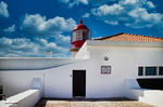 Faro blanco y rojo en la costa de Lagos con arquitectura sencilla y cielo azul con nubes.