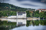 Edificio blanco reflejado en el río Moldava con colinas verdes de Praga al fondo.
