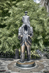 Estatua urbana de Franz Kafka en Praga rodeada de vegetación.